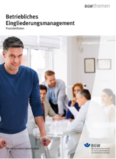 Foto: Links groß mittelalter Kollege in blauem Shirt mit 2 Krücken blickt freundlich in die Kamera. Im Hintergrund 5 Kolleg*innen an einem Tisch sitzend.