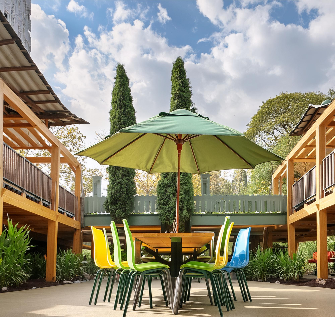 Tisch im Sommergarten mit grünem Sonnenschirm, darum bunte Stühle, Rechts und Links Holzveranden